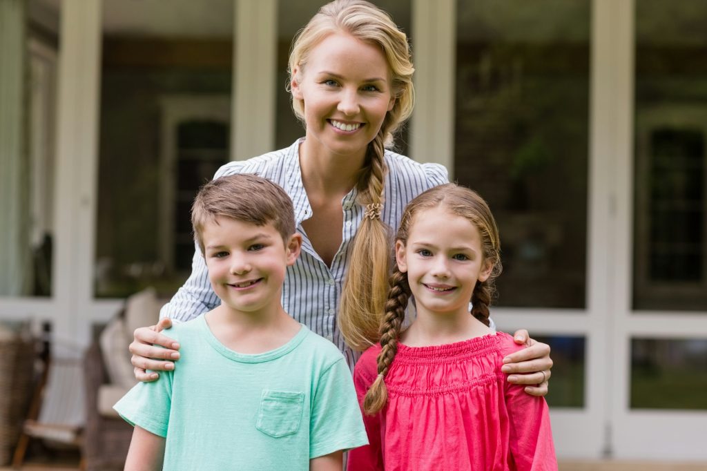 Smiling mother and kids standing outside home